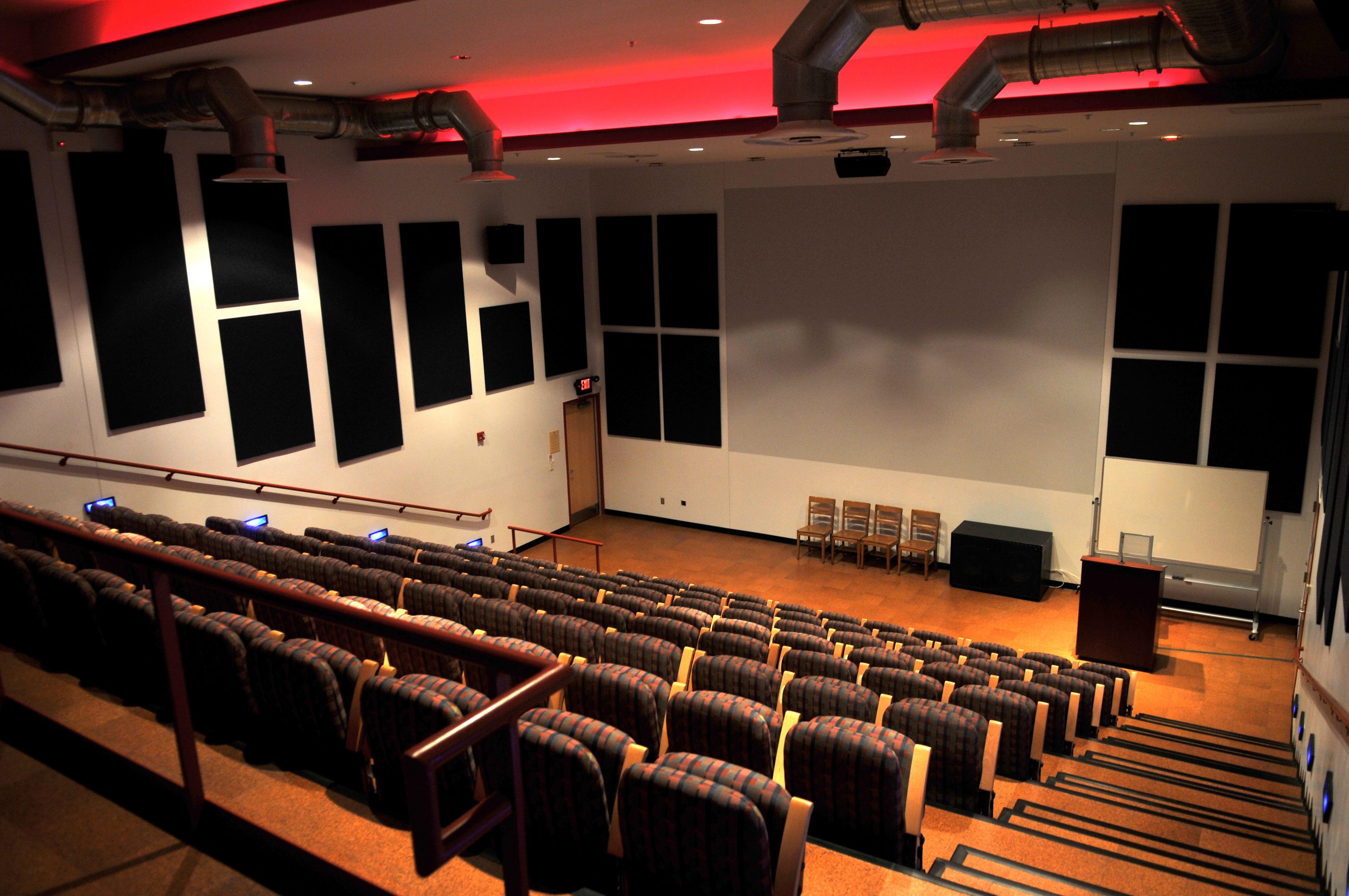 Image of an empty room with tiered chairs facing four chairs and a podium at the front 
