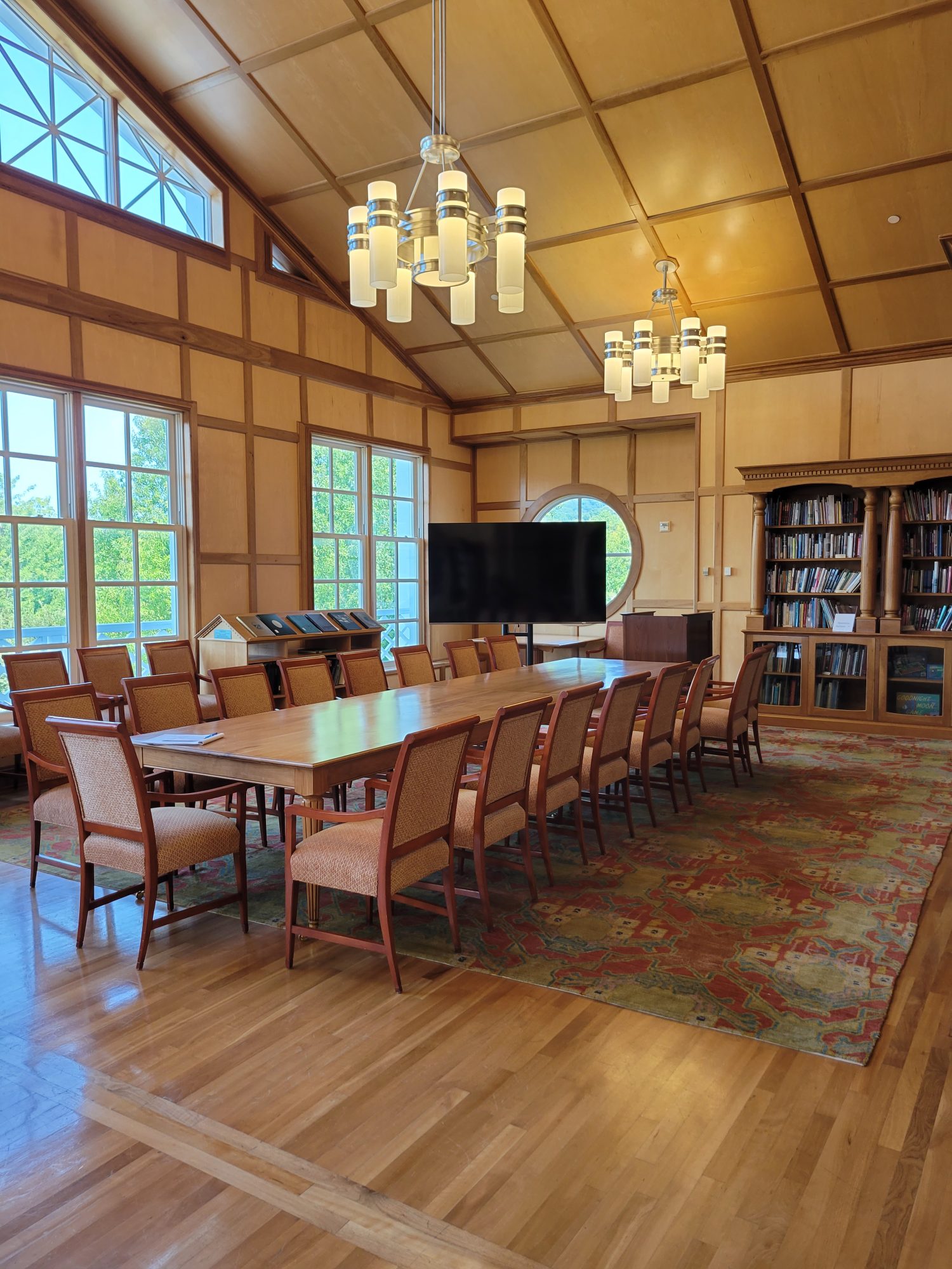 A room with large windows featuring a large table with chairs and a TV.