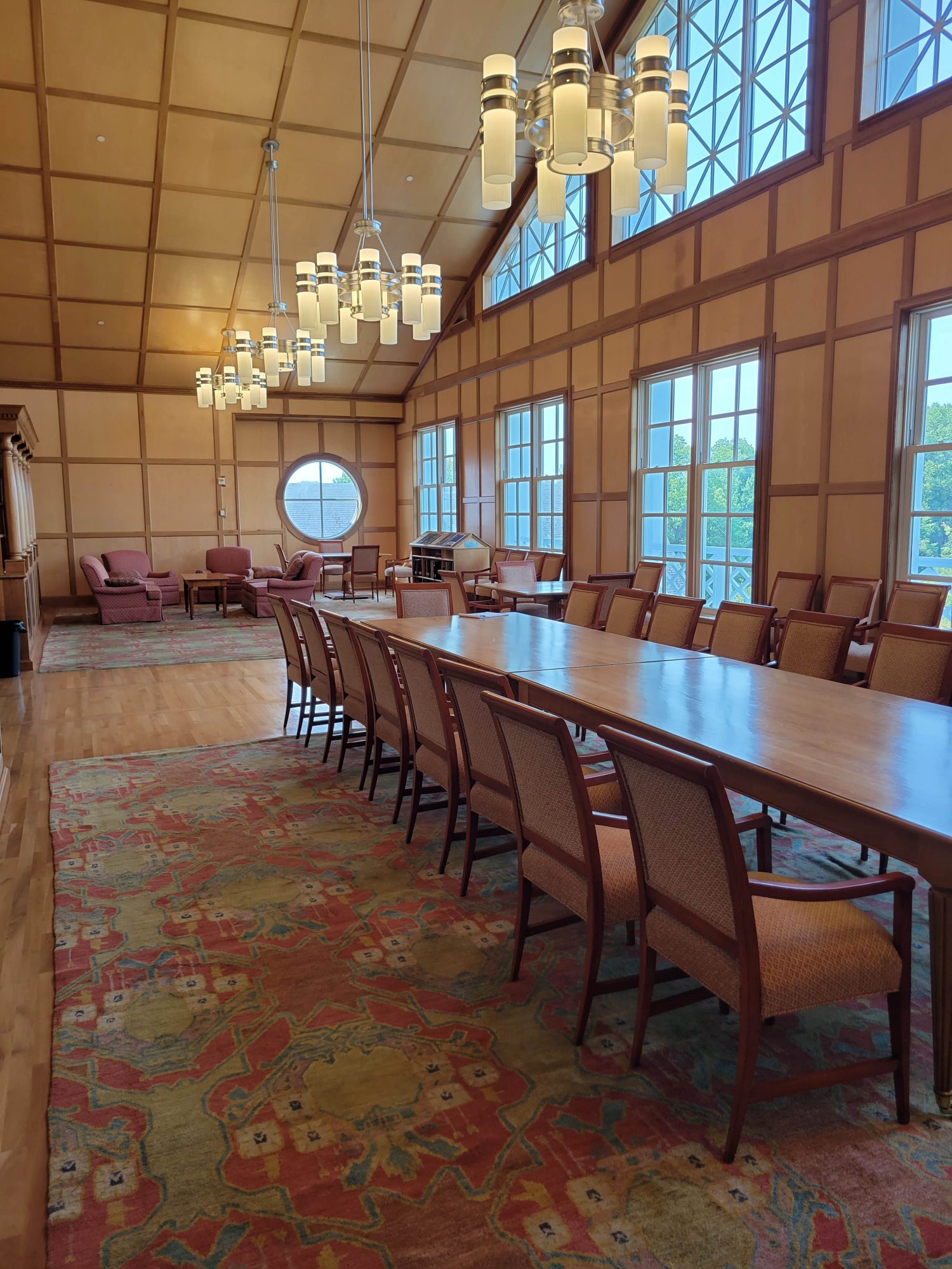 An image of a room with large windows, chandeliers, and a large conference table with chairs in the middle of the room.
