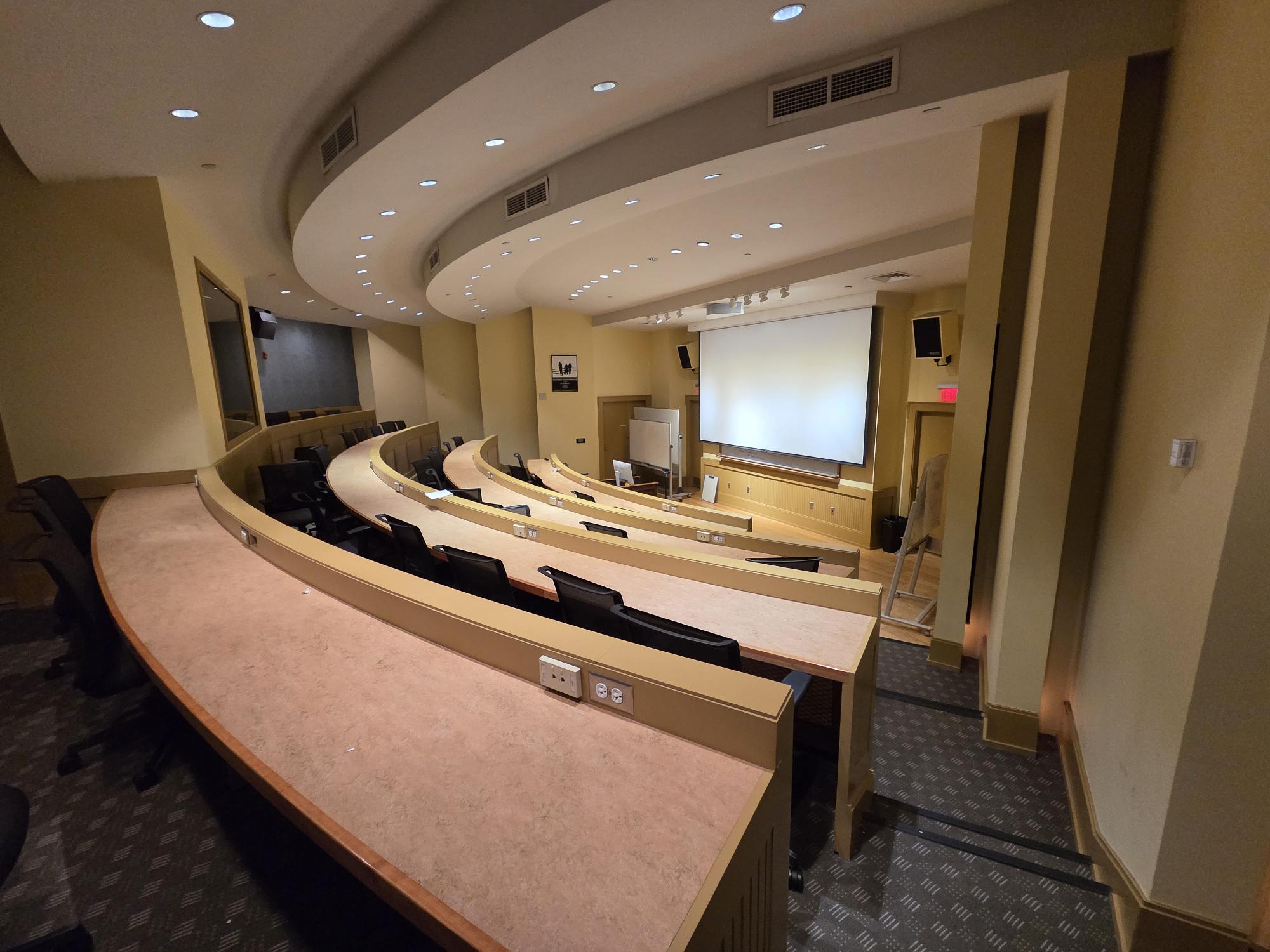 From the top of a small auditorium facing down towards the front of a room with screen. 