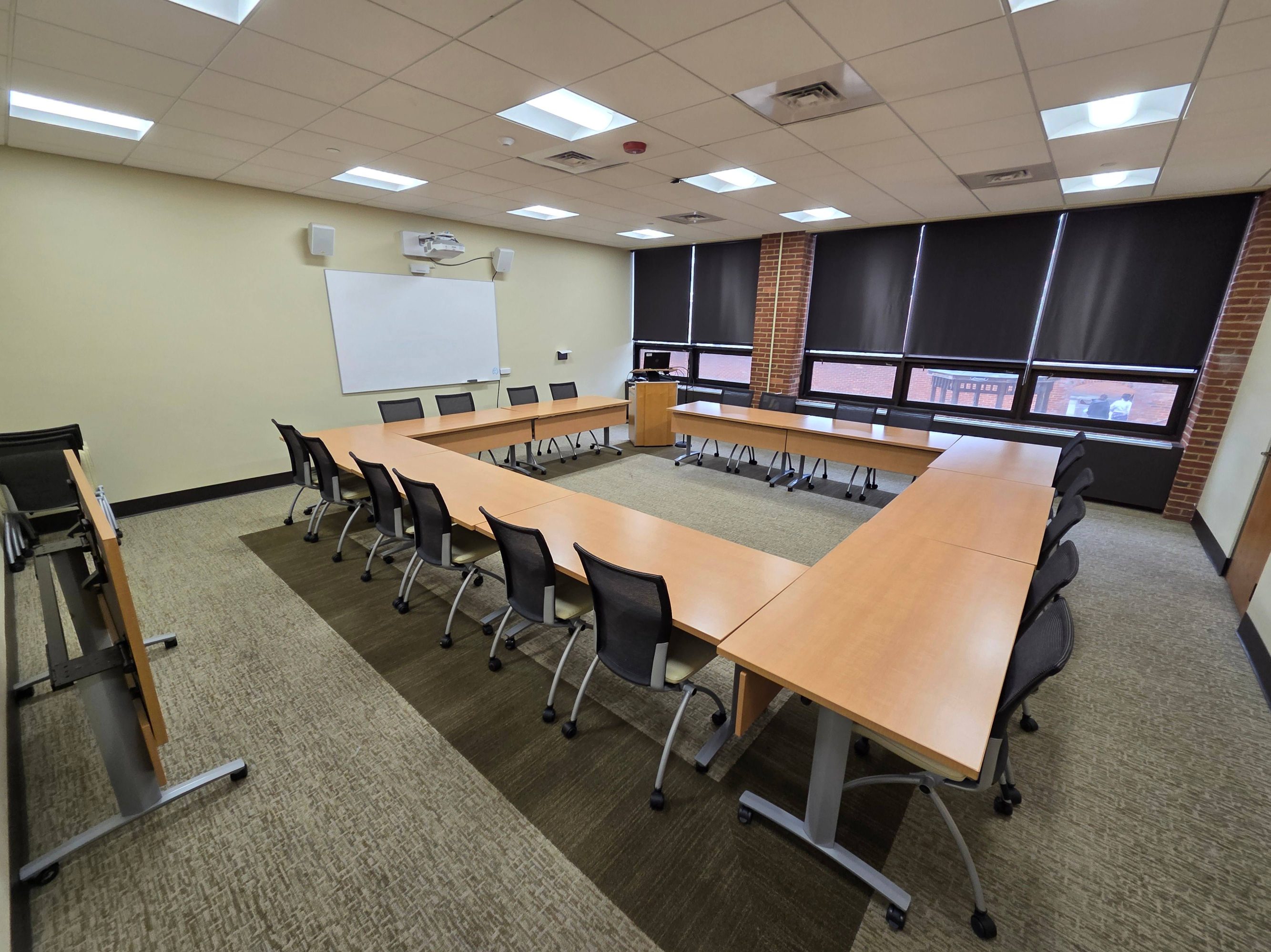 An image of Janney Lounge with 20 chairs sitting around a square table with a projector and screen and podium.