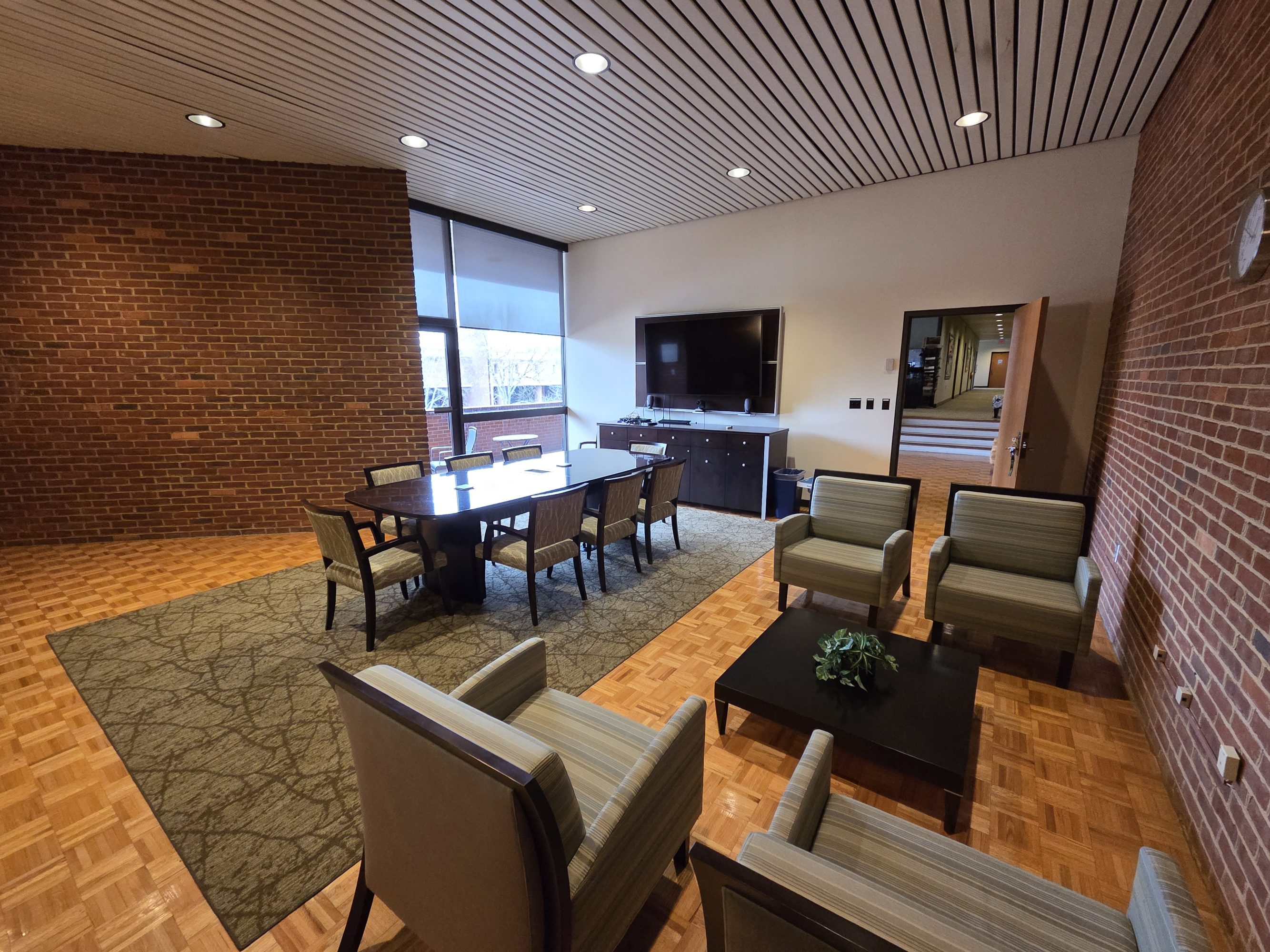  A small conference room with a table and chairs in the center and a seating area of four chairs on the right. 