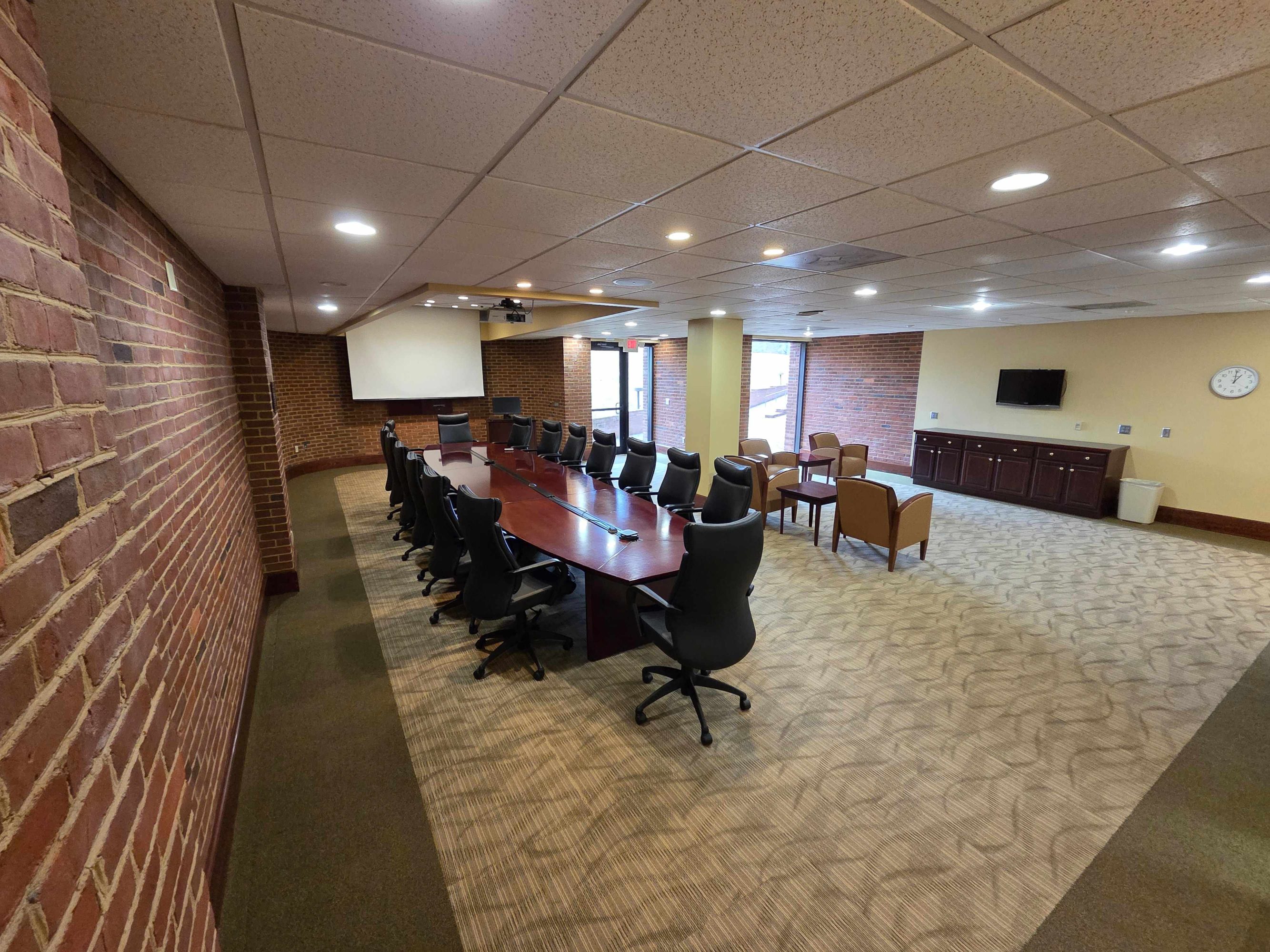 A conference room with several chairs around a large table and a small seating section on the right side. 