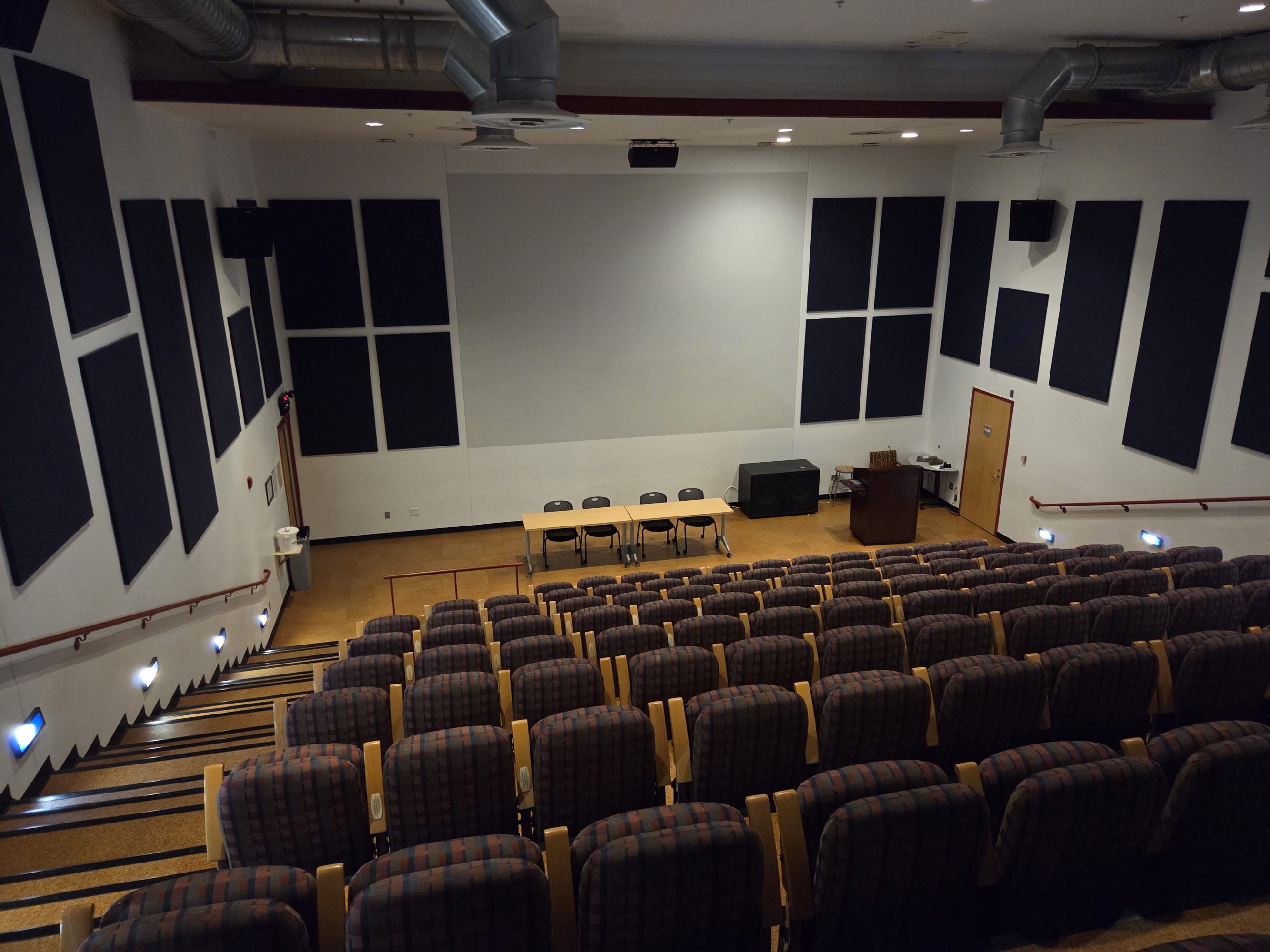 An image of an empty room of tiered chairs facing a long table with four chairs behind it.